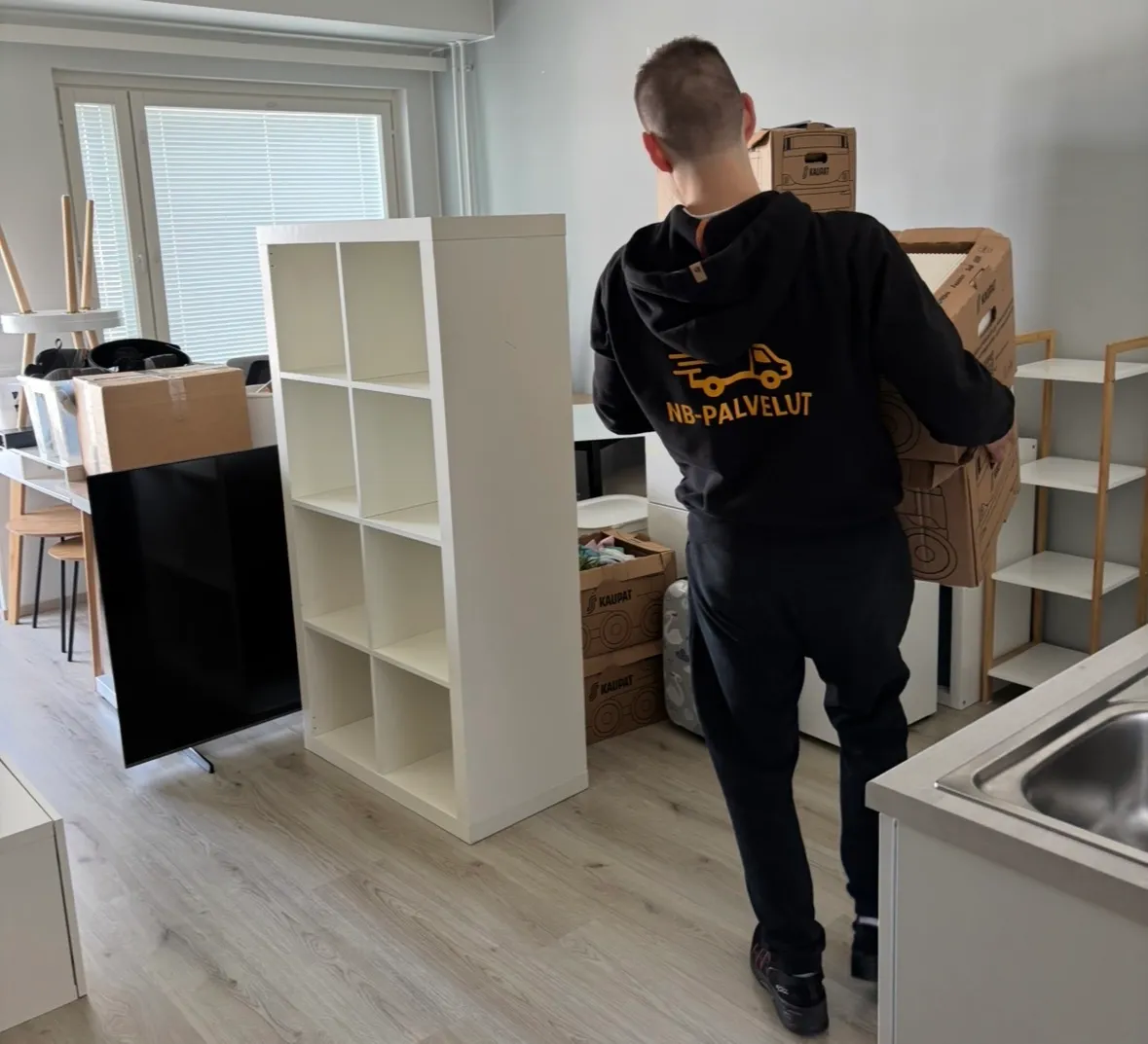 An NB-Palvelut mover carrying moving boxes in a customer's home